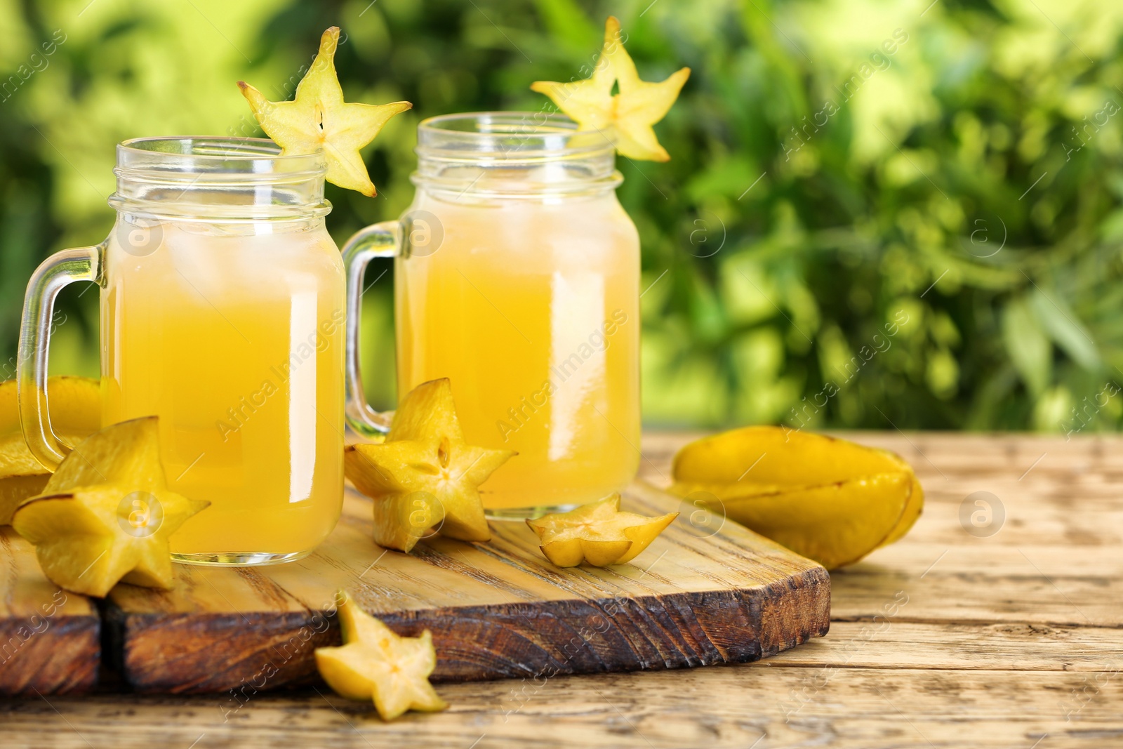 Photo of Delicious carambola juice and fresh fruits on wooden table against blurred background. Space for text