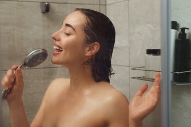 Photo of Washing hair. Happy woman with showerhead singing indoors, view through wet glass