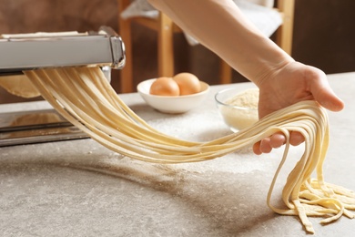 Photo of Young woman preparing noodles with pasta maker at table