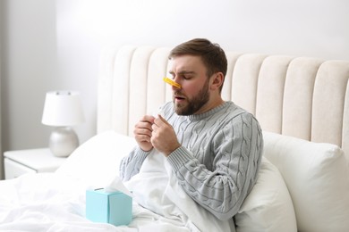 Photo of Young man with clothespin suffering from runny nose in bed indoors