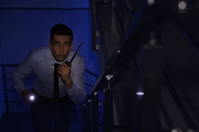 Male security guard with flashlight and portable radio transmitter in dark room