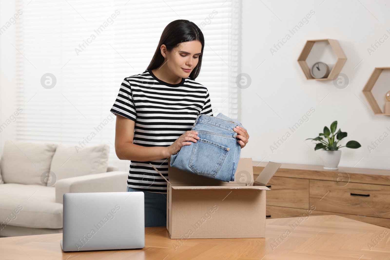 Photo of Young woman with just unpacked new jeans at wooden table indoors. Online shopping