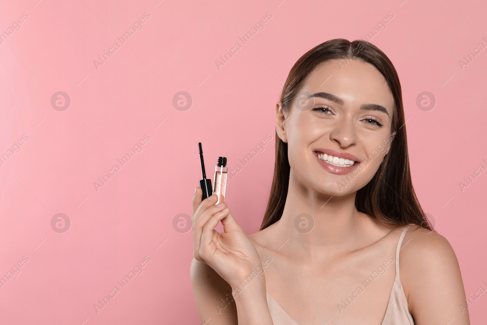 Photo of Young woman with eyelash oil on pink background, space for text