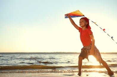 Photo of Cute little child playing with kite on beach near sea at sunset. Spending time in nature