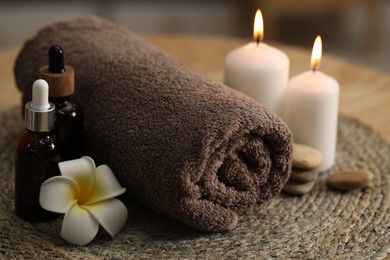 Photo of Spa composition. Rolled towel, cosmetic products, stones, burning candles and plumeria flower on table, closeup