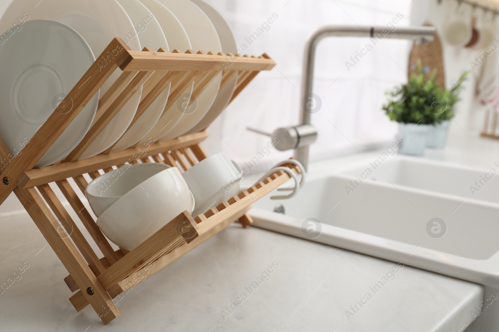 Photo of Drying rack with clean dishes on light marble countertop near sink in kitchen