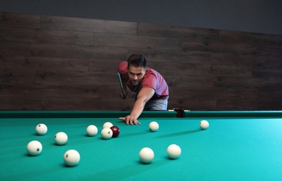 Handsome young man playing Russian billiard indoors