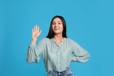 Photo of Happy woman waving to say hello on light blue background