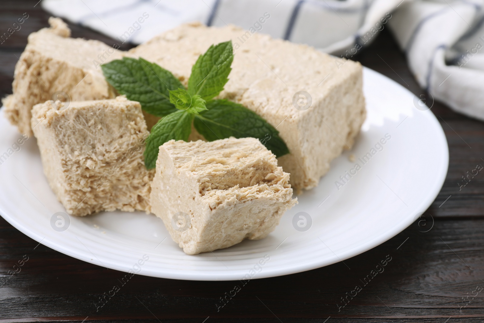 Photo of Plate with pieces of tasty halva and mint on wooden table, closeup