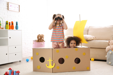 Photo of Cute little children playing with cardboard ship and binoculars at home