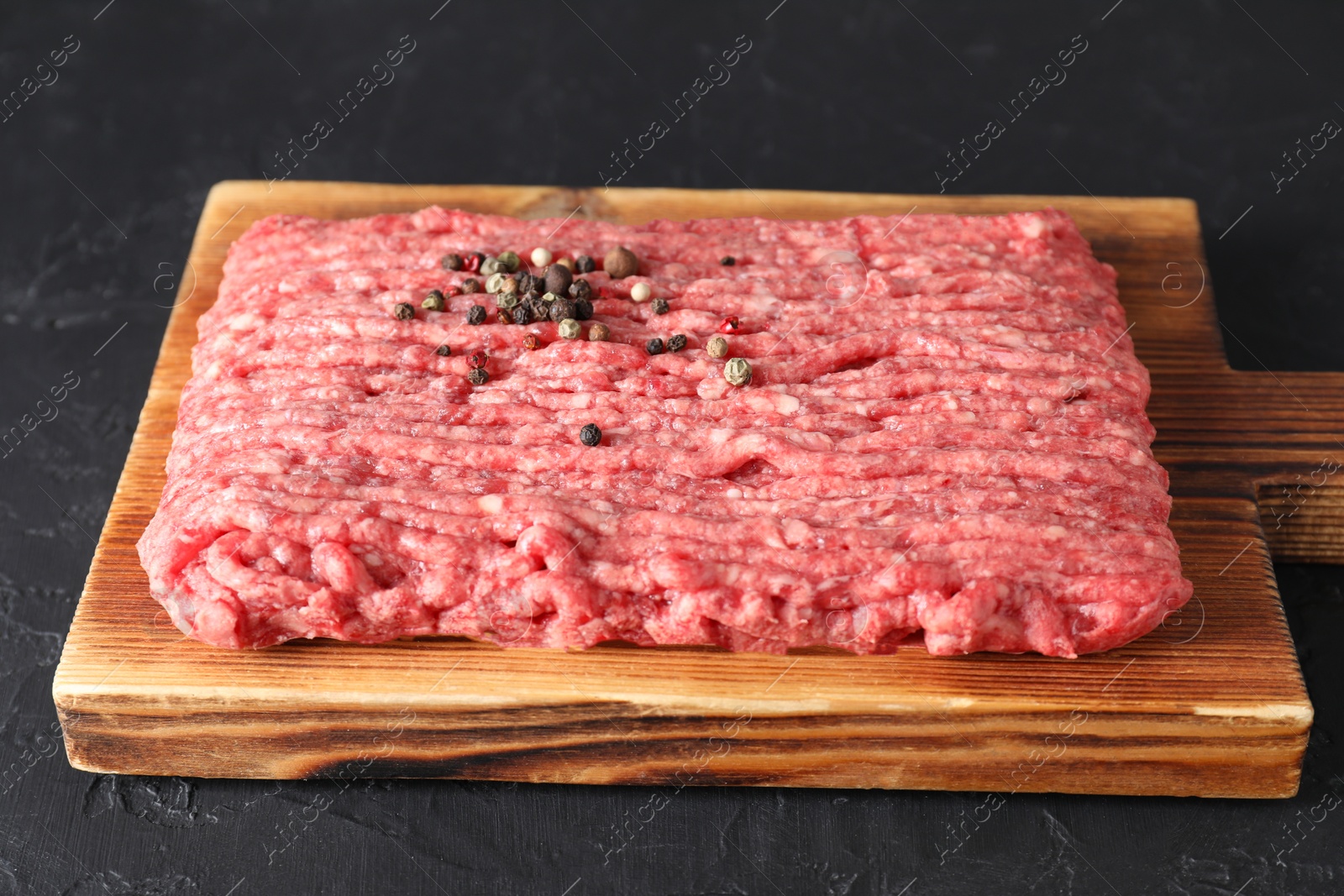 Photo of Raw ground meat and peppercorns on black table