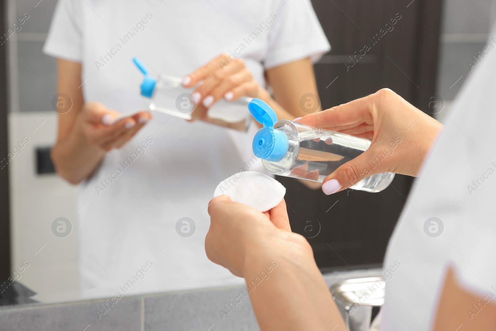 Photo of Woman pouring micellar water onto cotton pad in bathroom, closeup