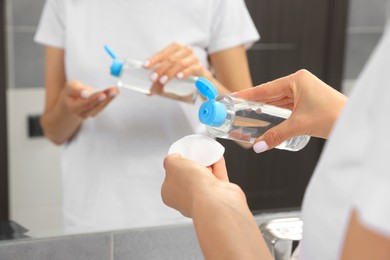 Photo of Woman pouring micellar water onto cotton pad in bathroom, closeup