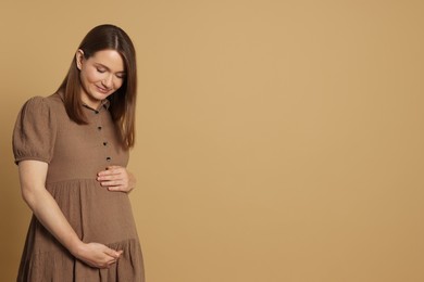 Photo of Happy young pregnant woman on light brown background. Space for text