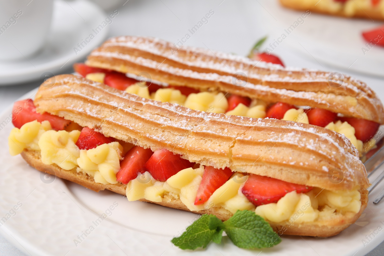 Photo of Delicious eclairs filled with cream, strawberries and mint on table, closeup