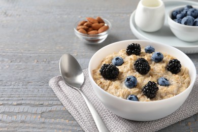 Photo of Tasty oatmeal porridge with blackberries and blueberries served on light grey wooden table