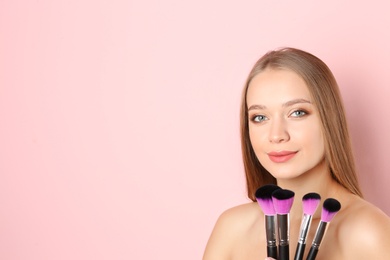 Portrait of beautiful young woman with makeup brushes on color background. Space for text