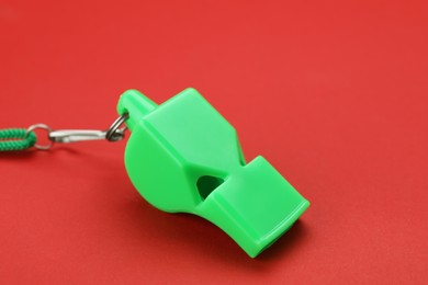 Photo of One green whistle with cord on red background, closeup