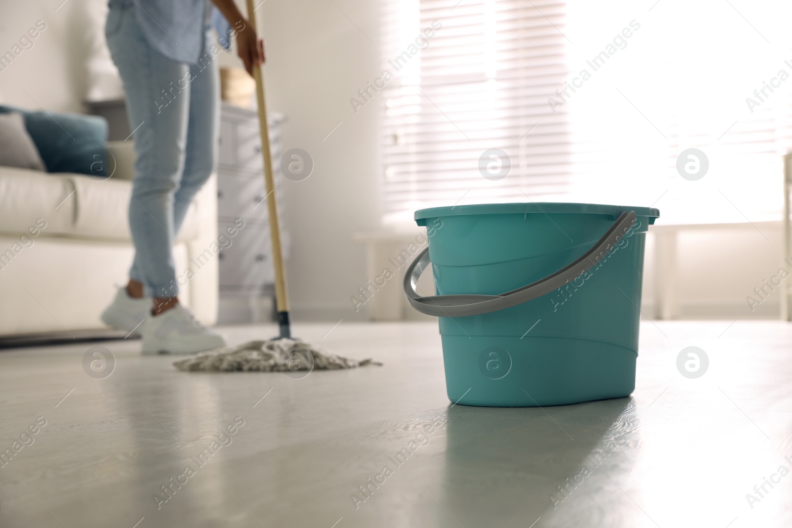 Photo of Plastic bucket and woman mopping floor in living room, closeup. Cleaning supplies