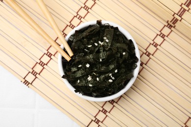 Photo of Chopped nori sheets, chopsticks and bamboo mat on white table, flat lay