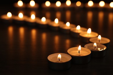 Photo of Burning candles on wooden table in darkness, closeup. Space for text