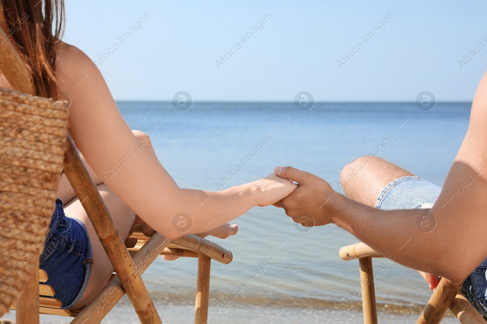 Photo of Young couple relaxing in deck chairs on beach near sea, closeup
