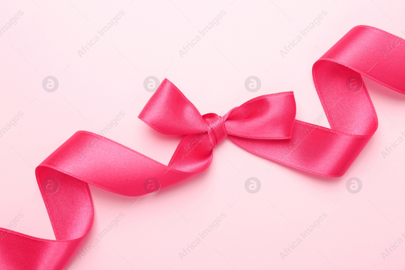 Photo of Pink ribbon with bow on color background, top view