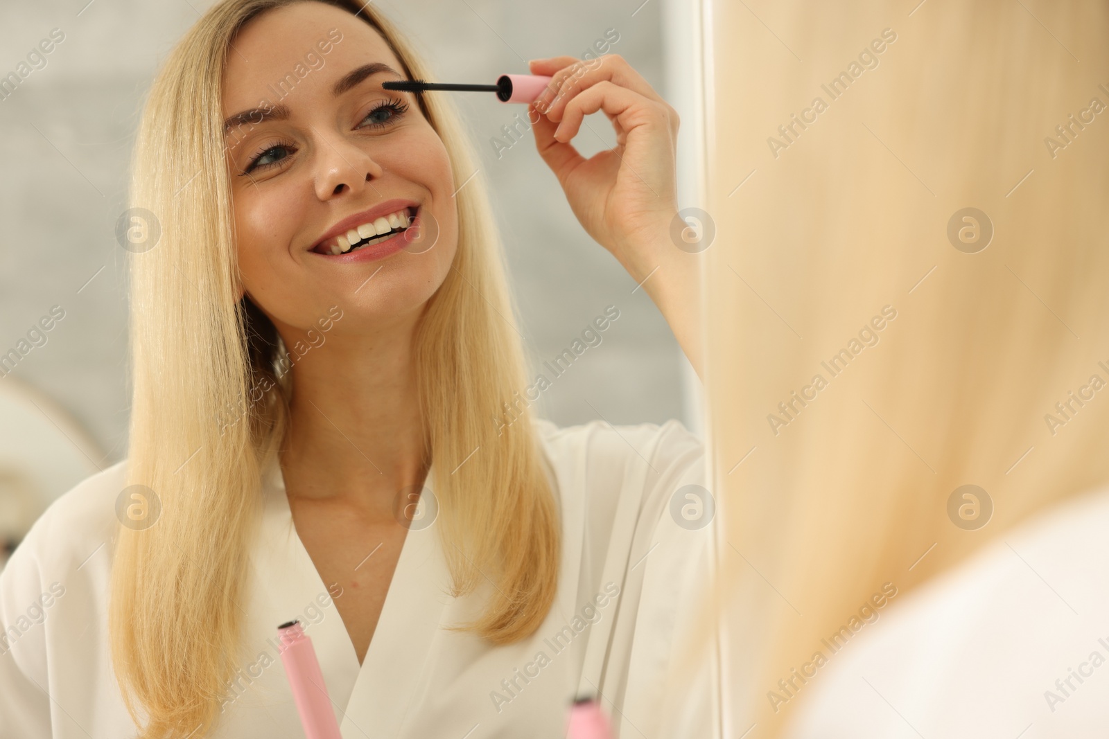 Photo of Beautiful woman applying mascara near mirror in bathroom