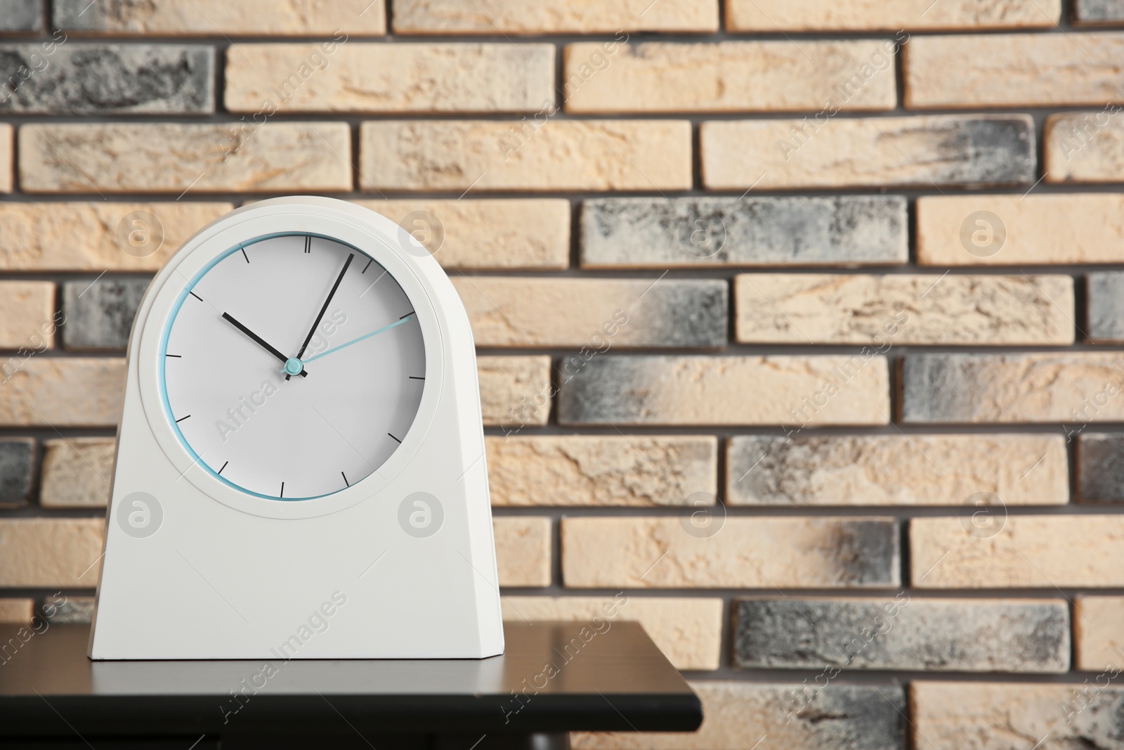 Photo of Stylish clock on table near brick wall. Time concept