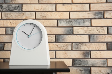 Photo of Stylish clock on table near brick wall. Time concept