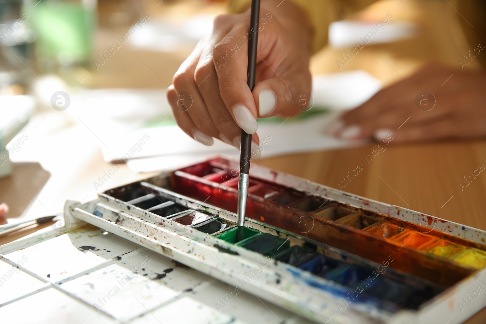 Photo of Young woman drawing with watercolors at table, closeup