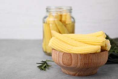 Tasty fresh yellow baby corns in bowl on grey table, space for text