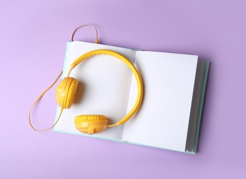 Photo of Modern headphones with open book on color background, top view