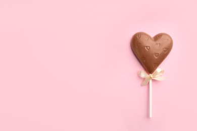 Chocolate heart shaped lollipop on light pink background, top view. Space for text
