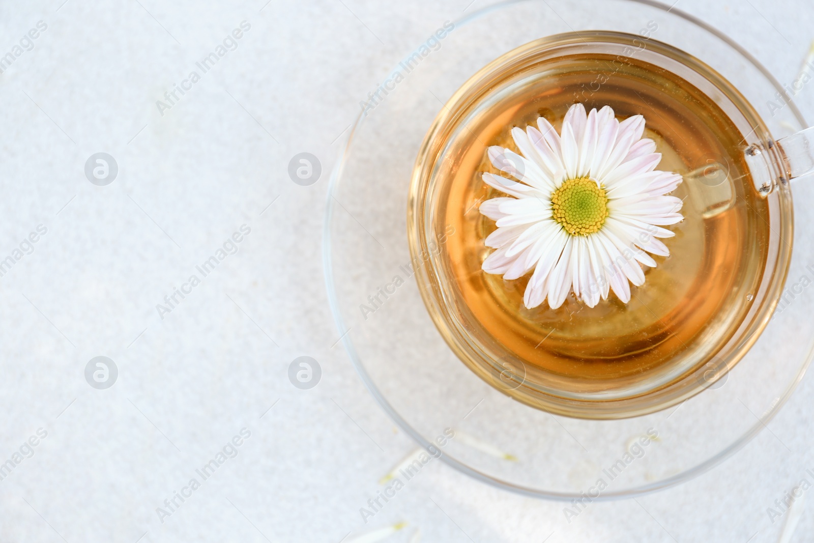 Photo of Glass cup of delicious chamomile tea on white table, top view. Space for text