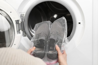 Photo of Woman putting stylish sneakers into washing machine, closeup