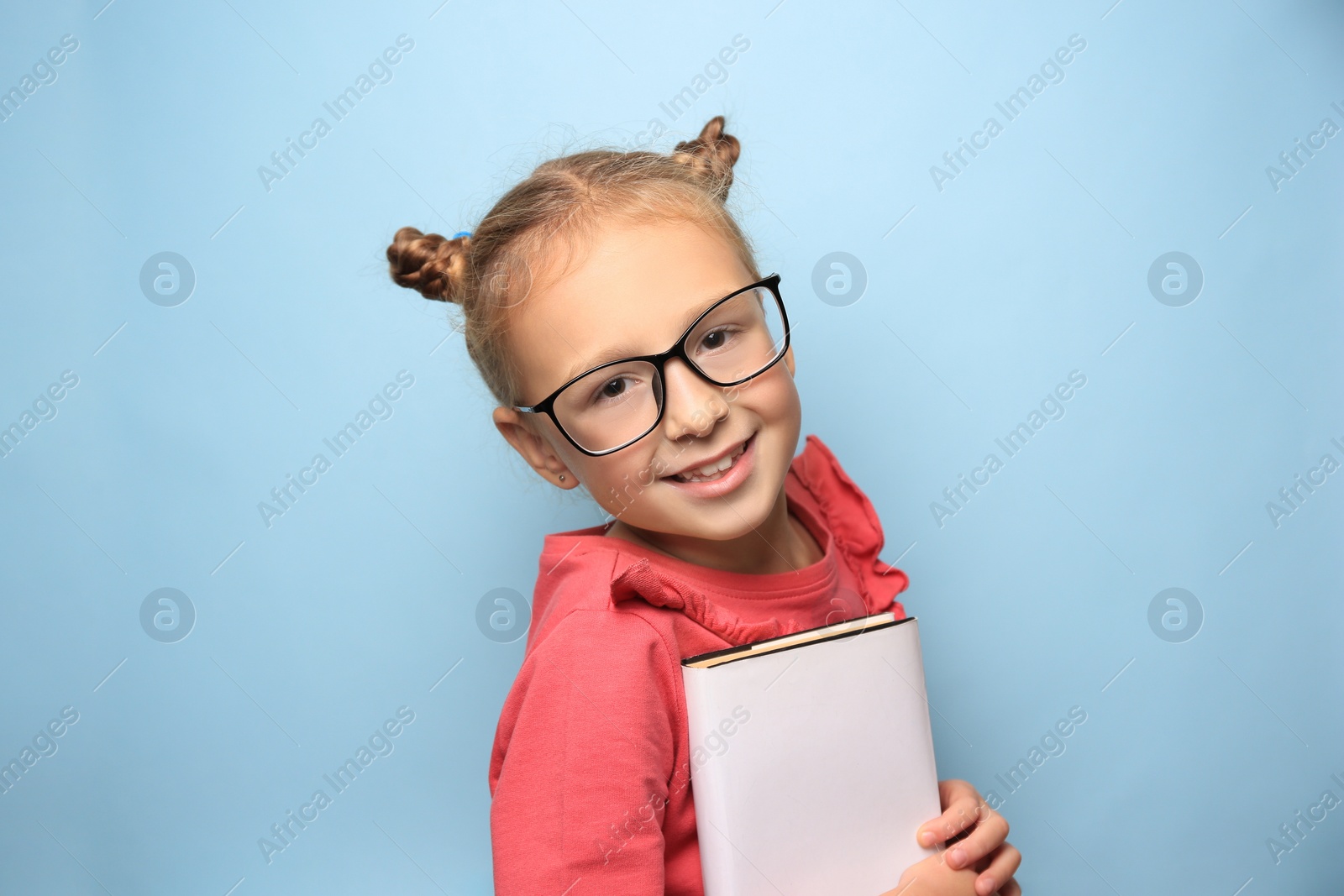 Photo of Cute little girl with glasses and textbook on light blue background