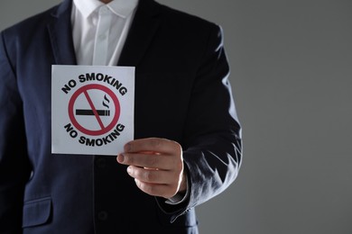 Photo of Man holding card with no smoking sign on gray background, closeup. Space for text