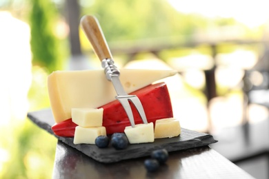 Different delicious cheeses, fork and blueberries on wooden railing outdoors