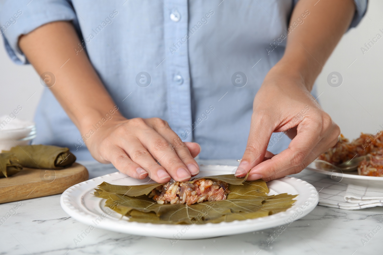 Photo of Woman preparing stuffed grape leaves at white marble table, closeup