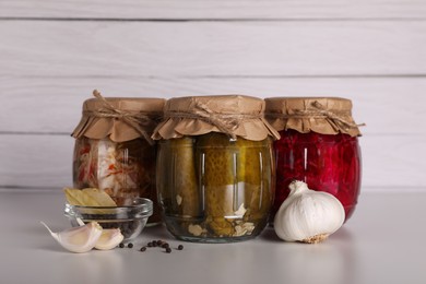 Jars with different preserved vegetables and fresh spices for canning on light grey table