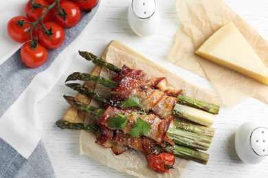 Photo of Oven baked asparagus wrapped with bacon on white wooden table, flat lay