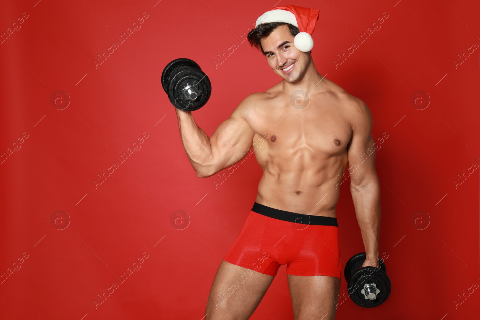 Photo of Sexy shirtless Santa Claus with dumbbells on red background