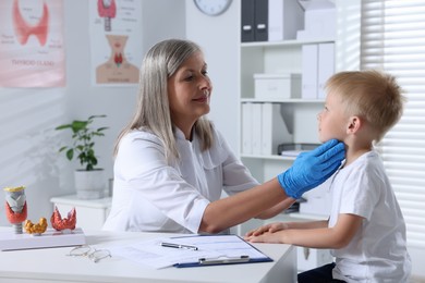 Endocrinologist examining boy's thyroid gland at table in hospital