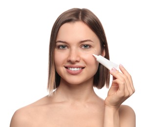 Photo of Young woman applying cream under eyes on white background