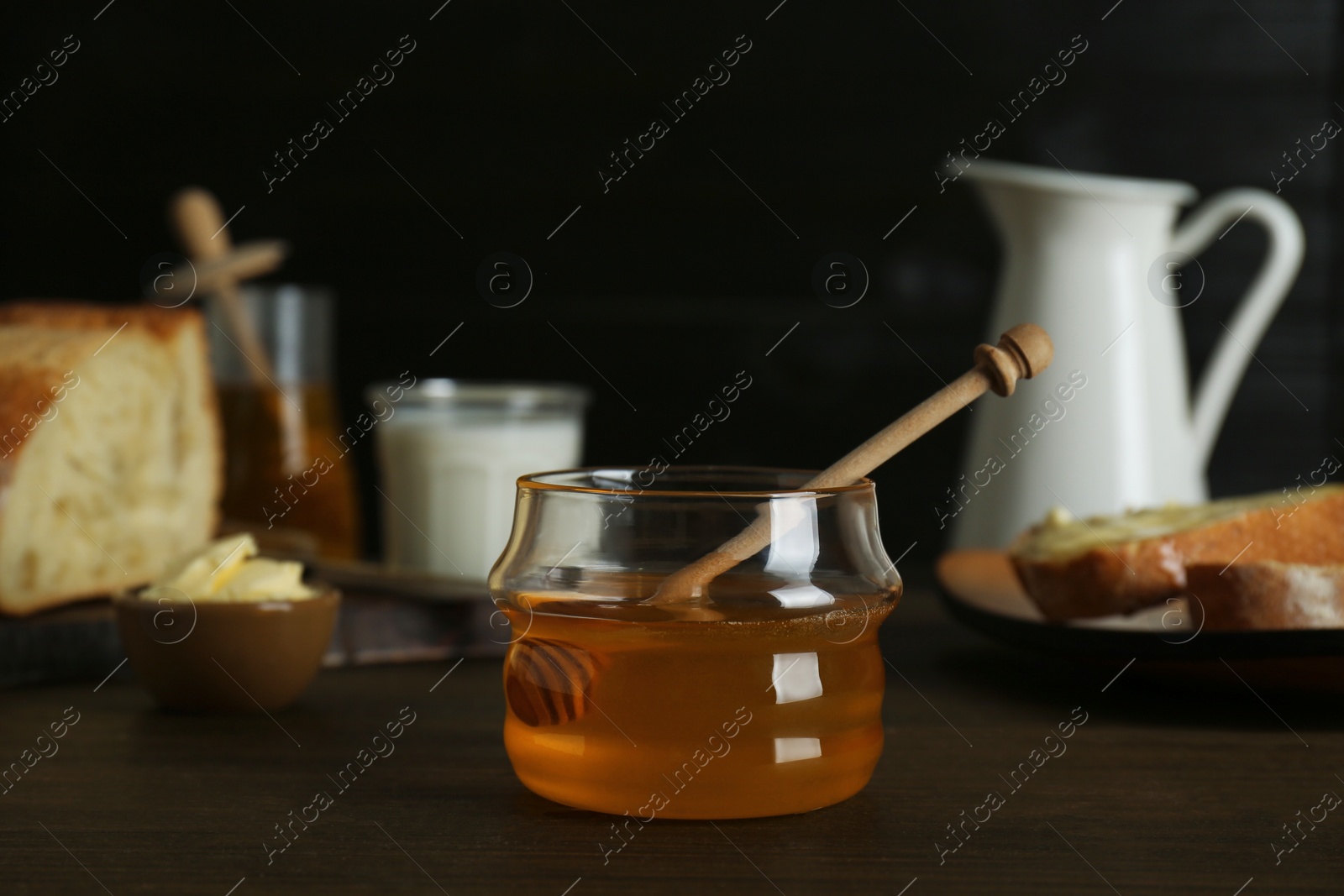 Photo of Jar with honey, milk, bread and butter on wooden table