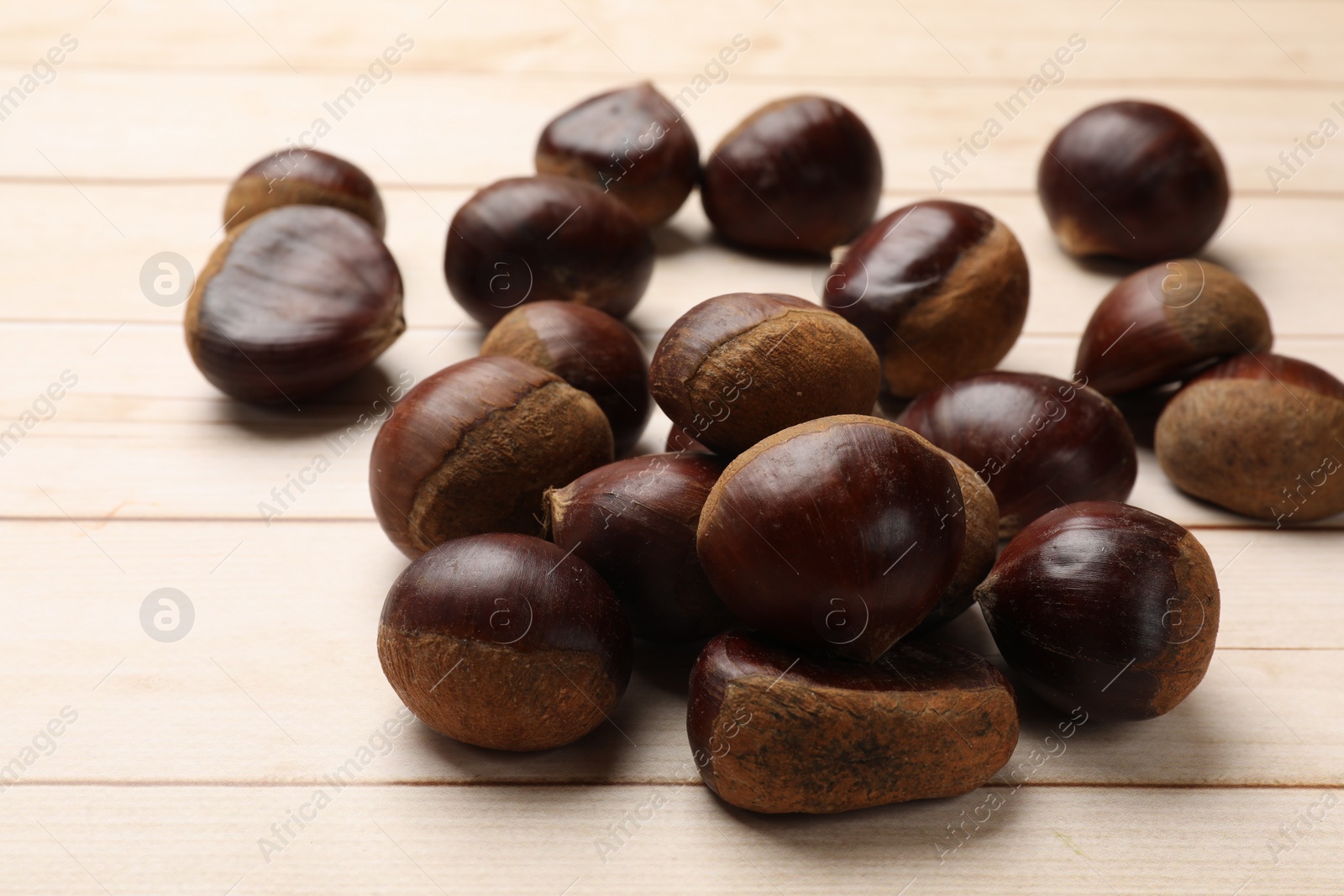 Photo of Sweet fresh edible chestnuts on light wooden table, closeup