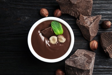 Photo of Dessert bowl with sweet chocolate cream, nuts and chunks on wooden table, flat lay