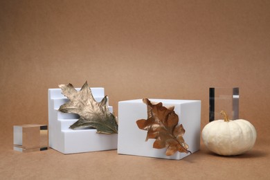 Photo of Autumn presentation for product. Geometric figures, golden leaves and pumpkin on light brown background