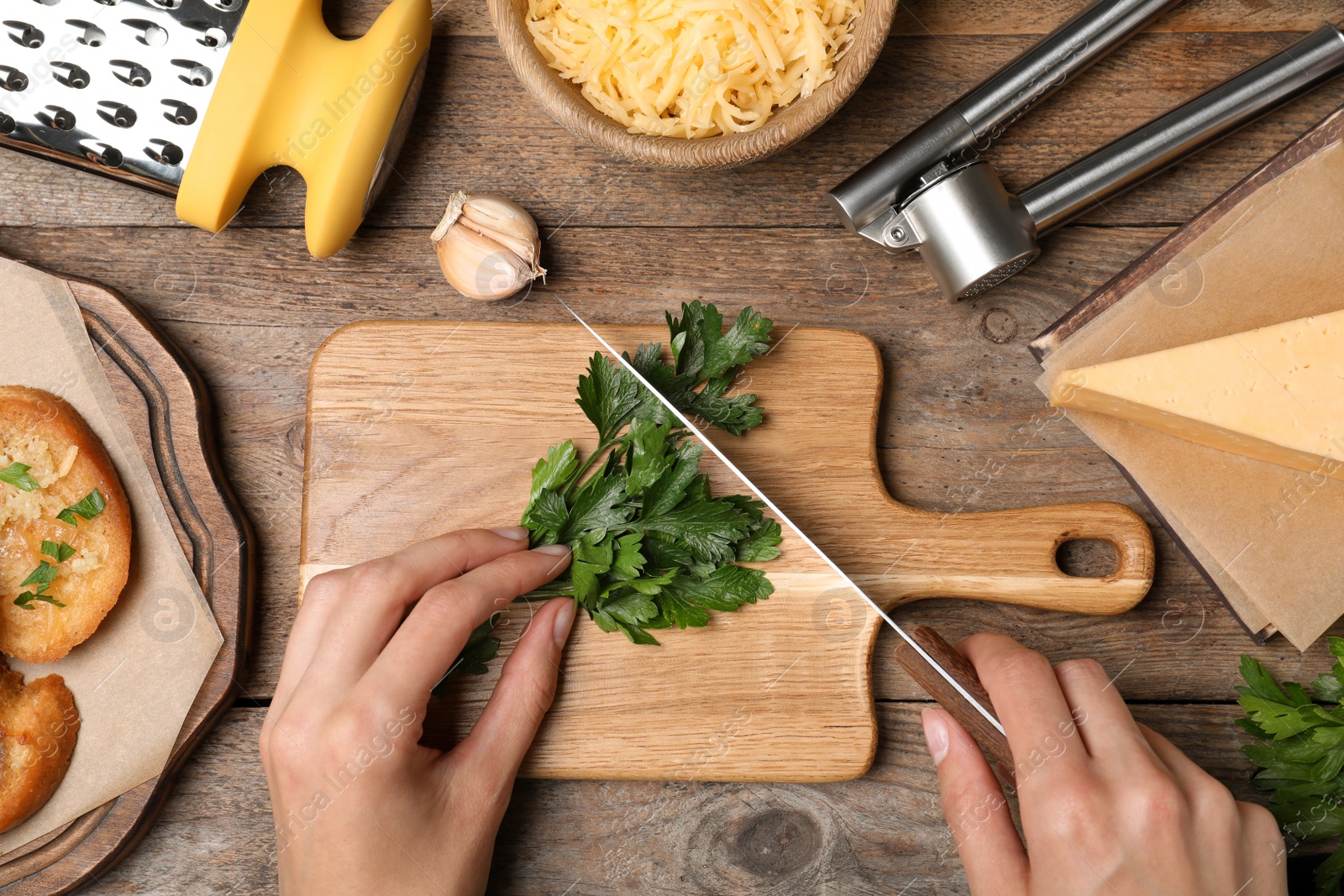 Photo of Woman cutting parsley for garlic bread at wooden table, top view